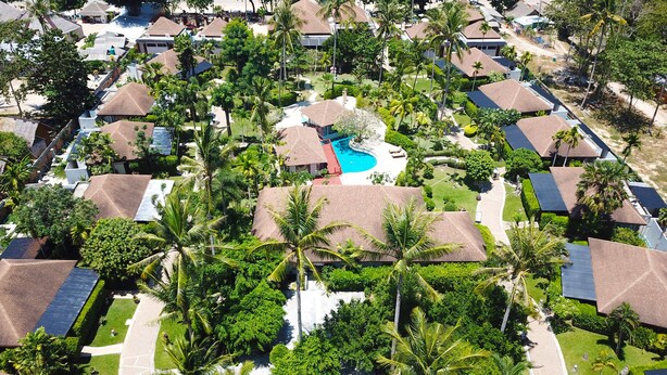 Vista aérea de un resort con varias construcciones tipo bungalow, una piscina central y exuberante vegetación tropical.