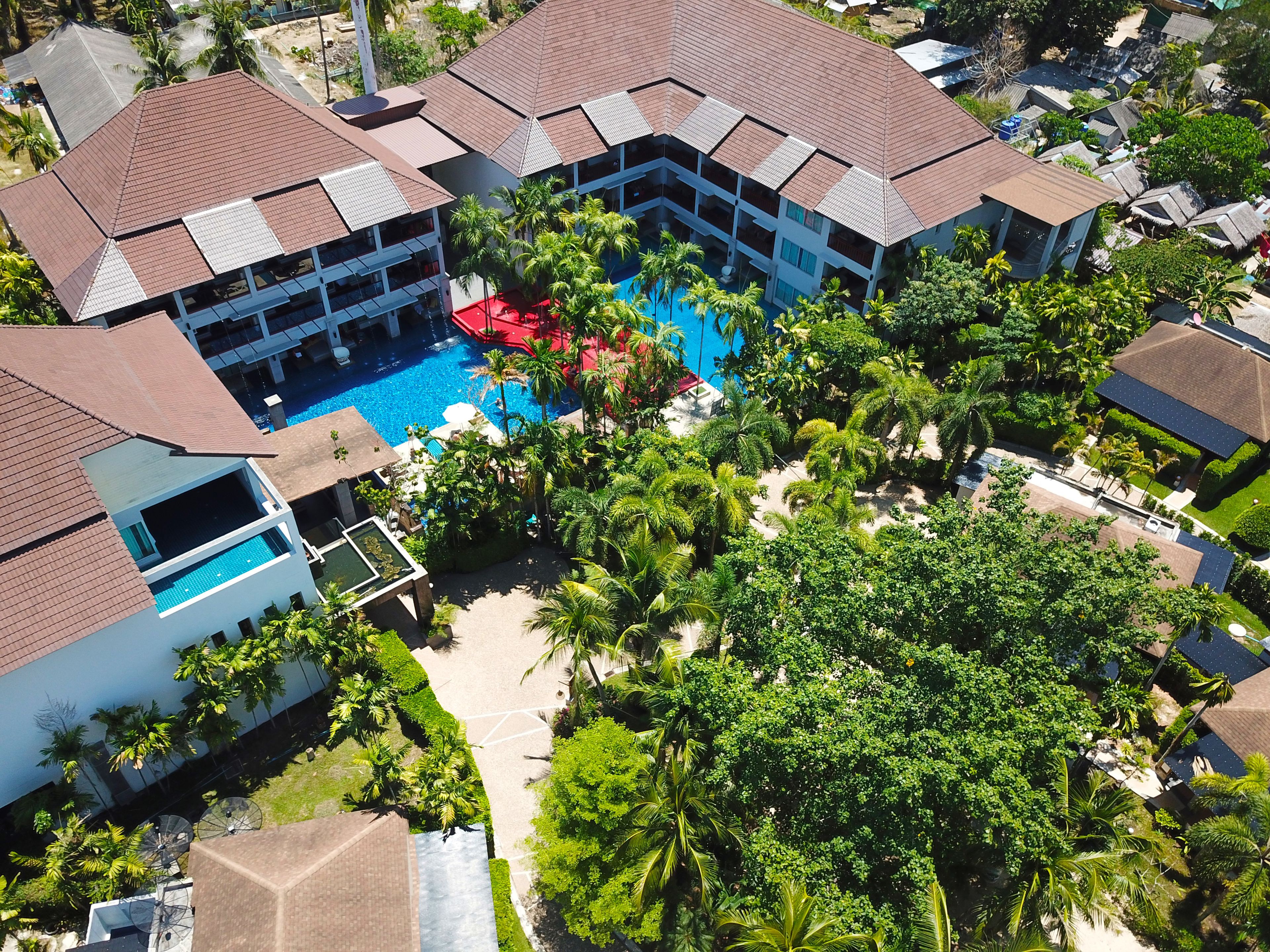Vista aérea de un resort con varias construcciones, una piscina central y abundante vegetación.
