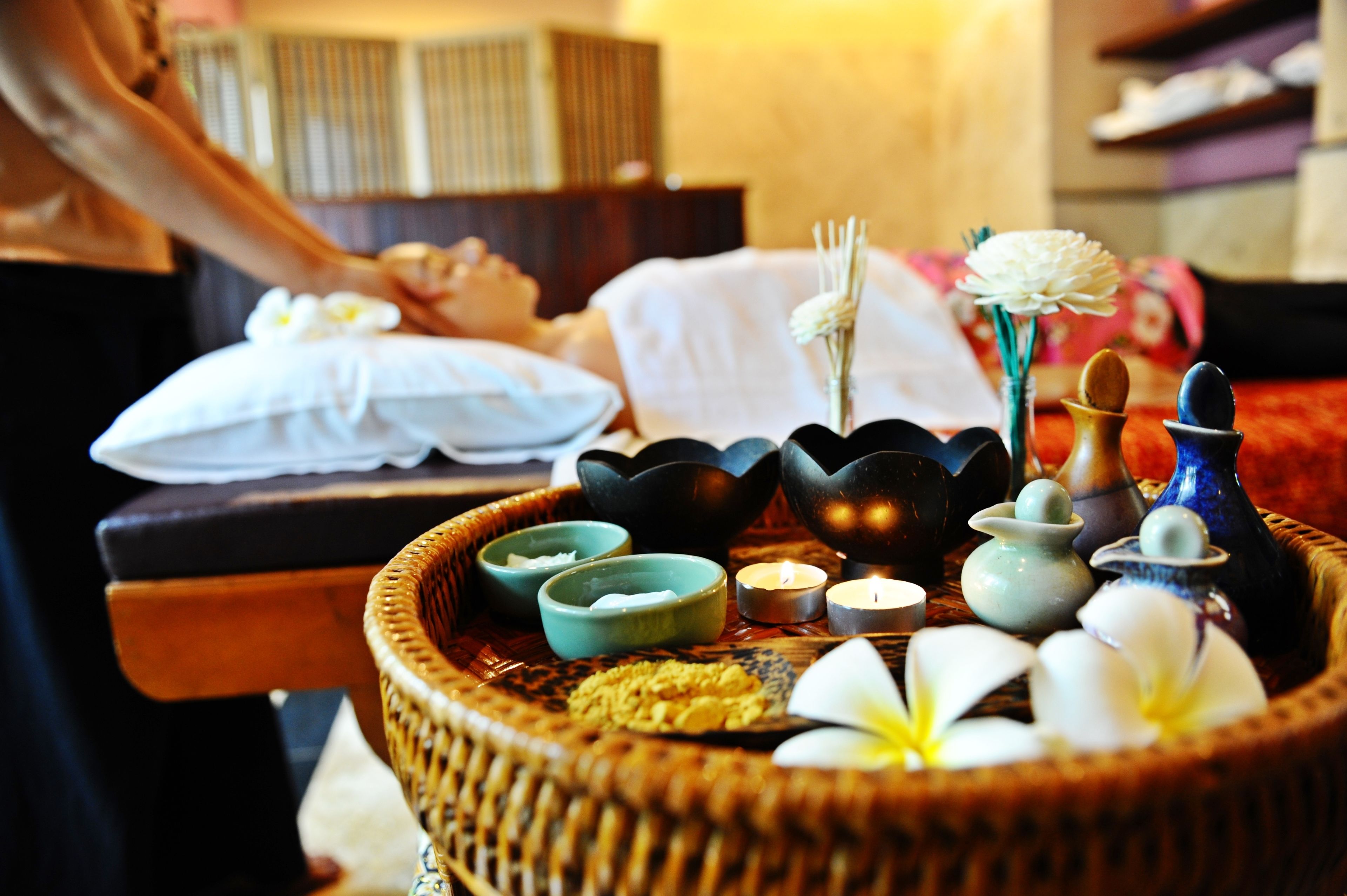 A spa setting with a wicker tray containing candles, small bowls, and flowers.