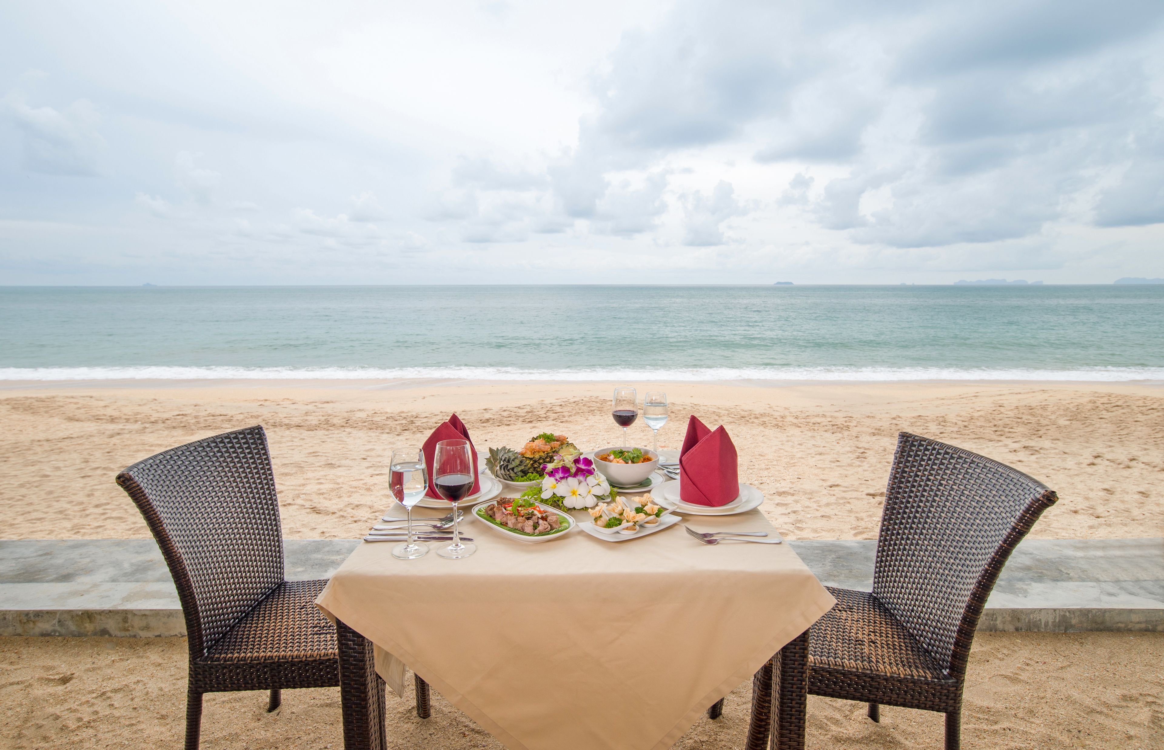 Ein Tisch am Strand mit Meerblick, zwei Korbstühle und eine Tischdecke.