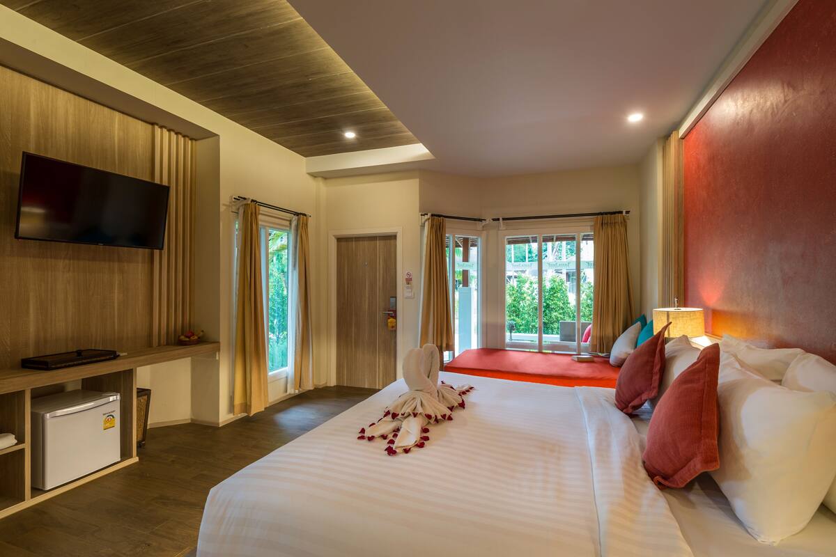 A hotel room with a bed, a flat-screen TV, a mini-fridge, and a view of the outdoors.