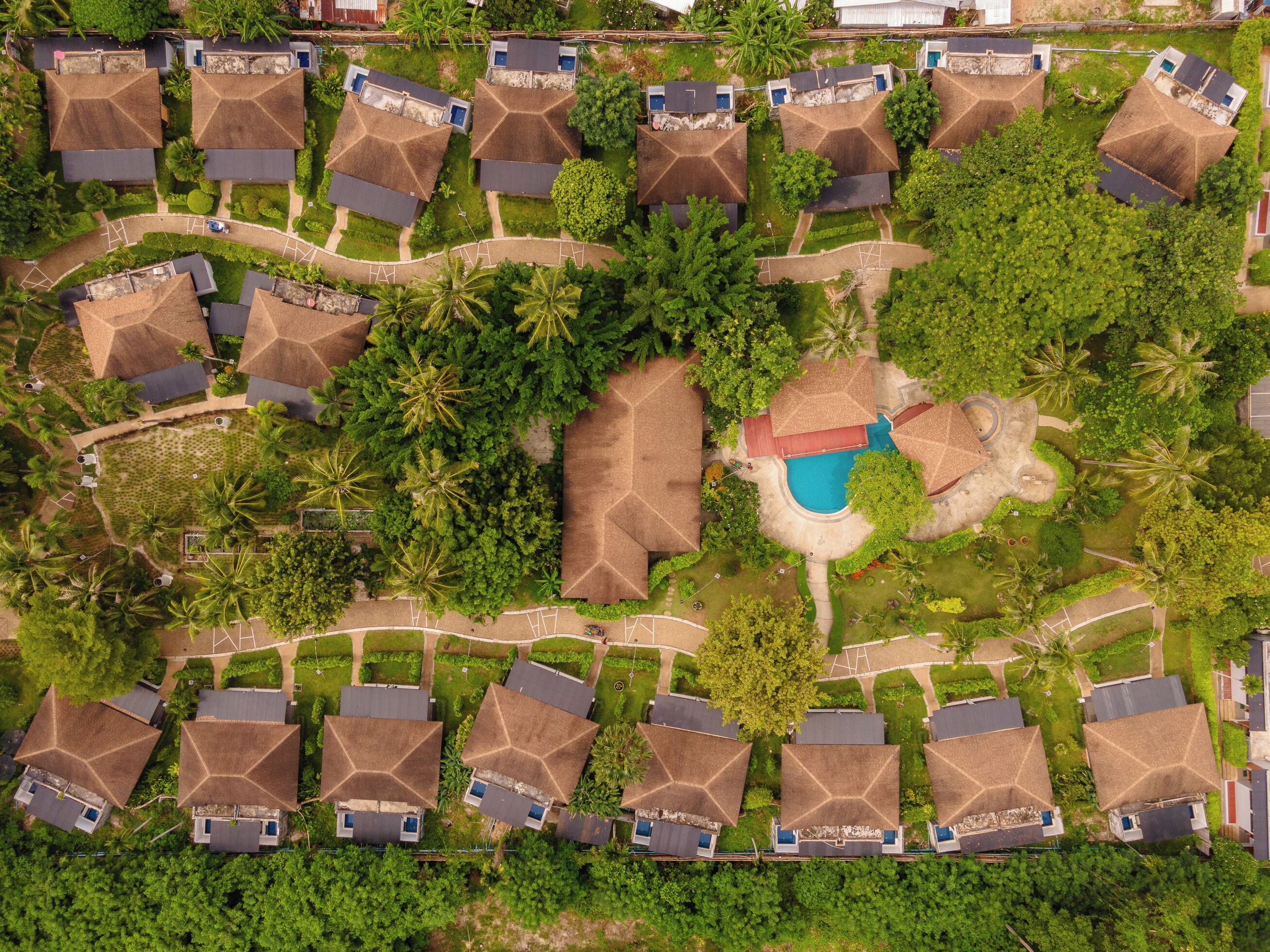 An aerial view of a resort with multiple bungalow-style buildings, a central swimming pool, and surrounding lush greenery.