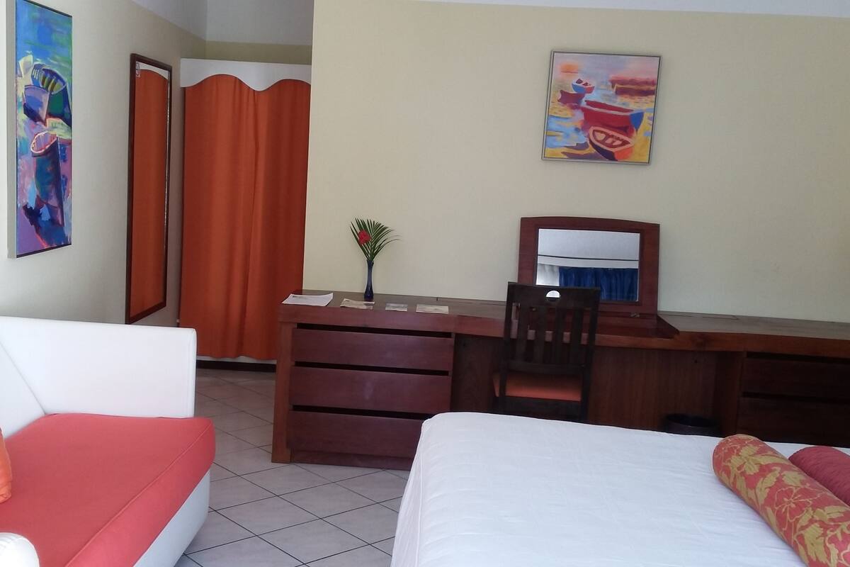 Habitación de hotel con cama, escritorio, silla, sofá, espejo y un cuadro en la pared.