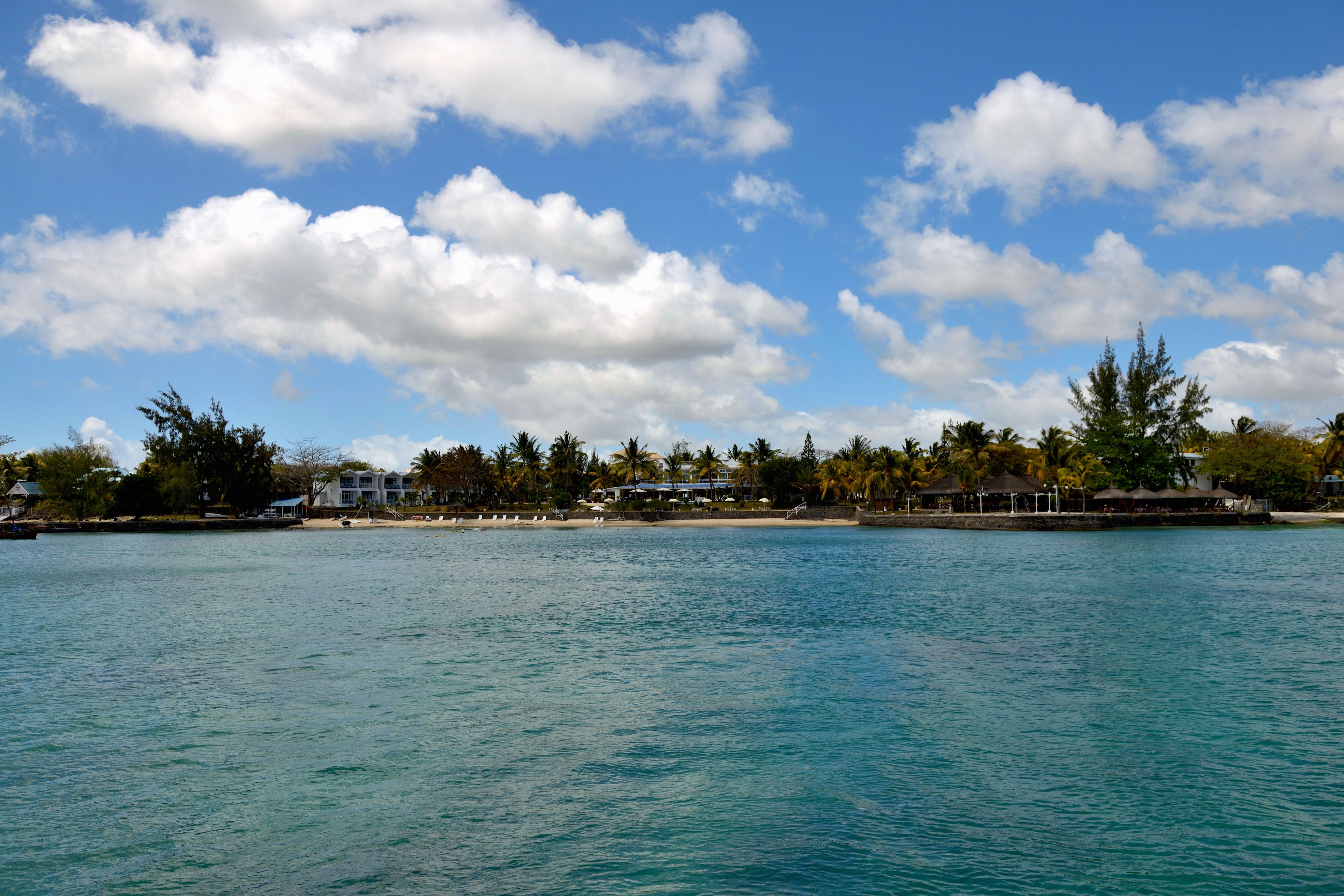 A coastal view with a clear sky, calm sea, and a row of buildings along the shore.