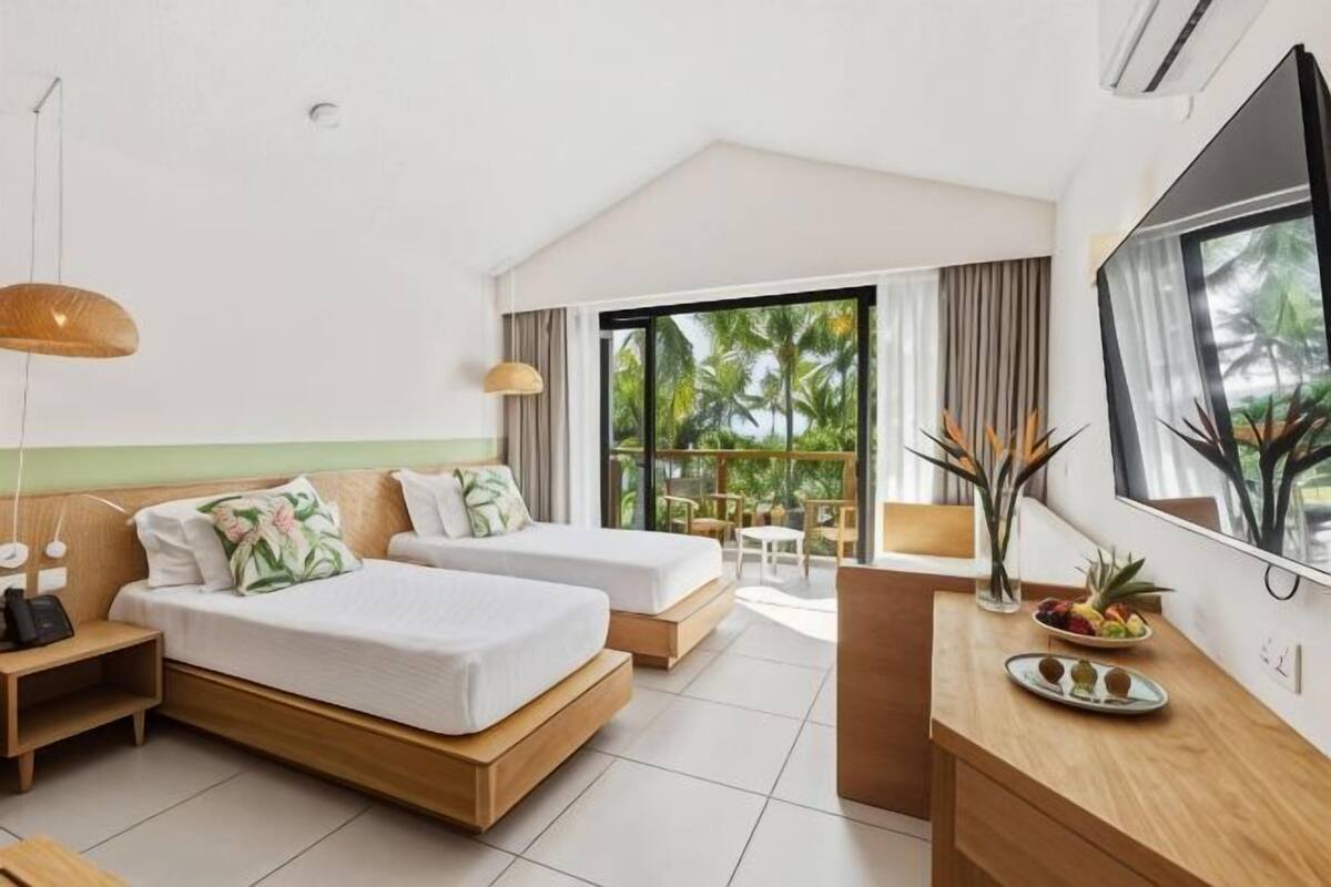 Una habitación de hotel moderna con una cama grande, un escritorio, un televisor y un balcón con vistas a palmeras.