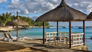 A beachside lounge with thatched umbrellas, lounge chairs, and a dining area overlooking the ocean. - Coral Azur Beach Resort (Mont Choisy)