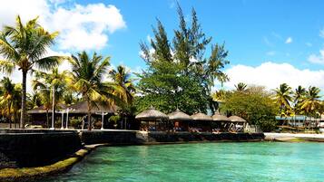 A tropical resort with clear turquoise water, palm trees, and thatched-roof structures.
