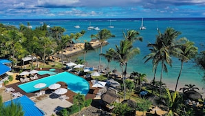 A resort with a swimming pool, lounge chairs, umbrellas, and a view of the ocean and boats. - Coral Azur Beach Resort (Mont Choisy)