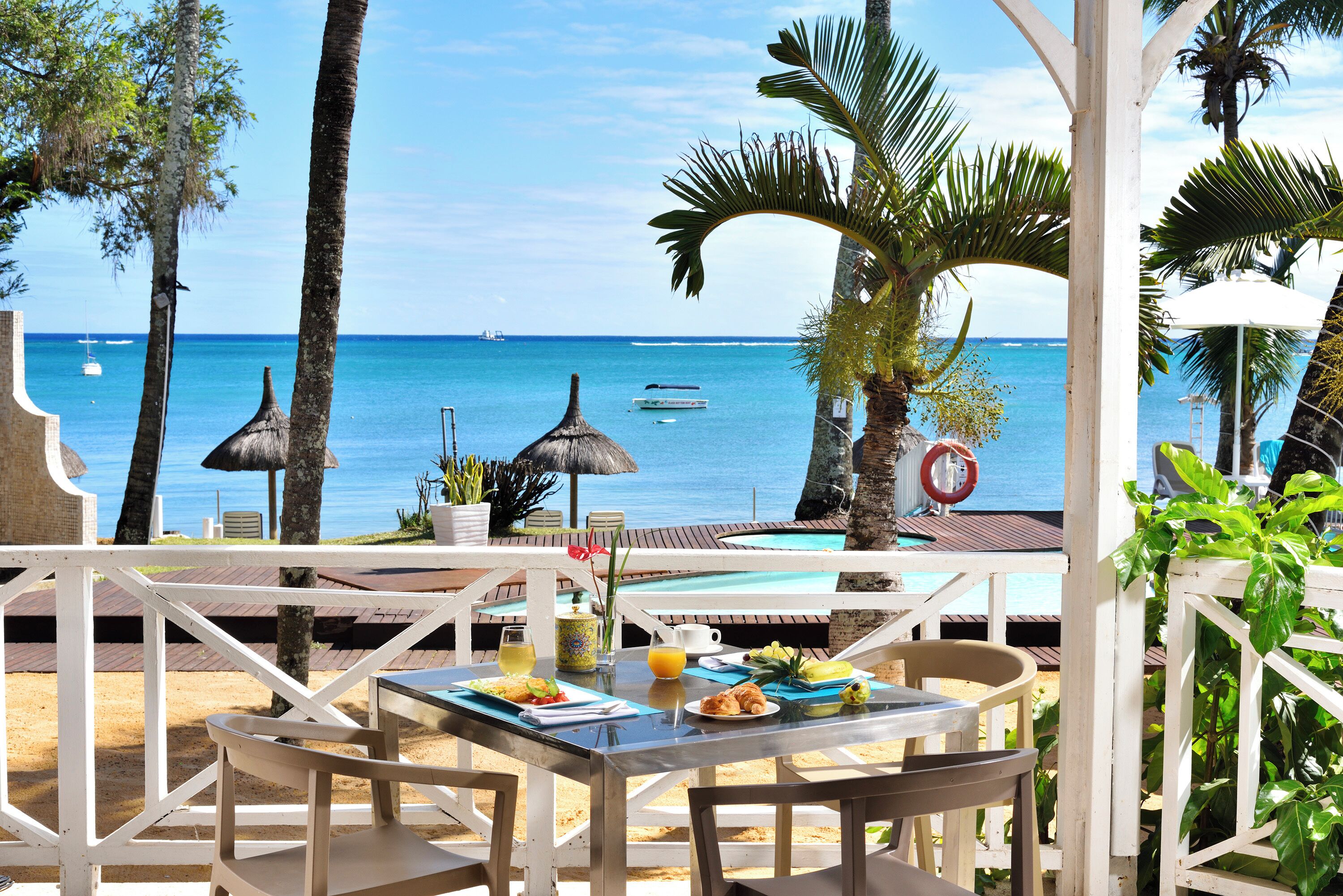 A beachside dining area with a table set for two, overlooking the ocean with boats in the distance.
