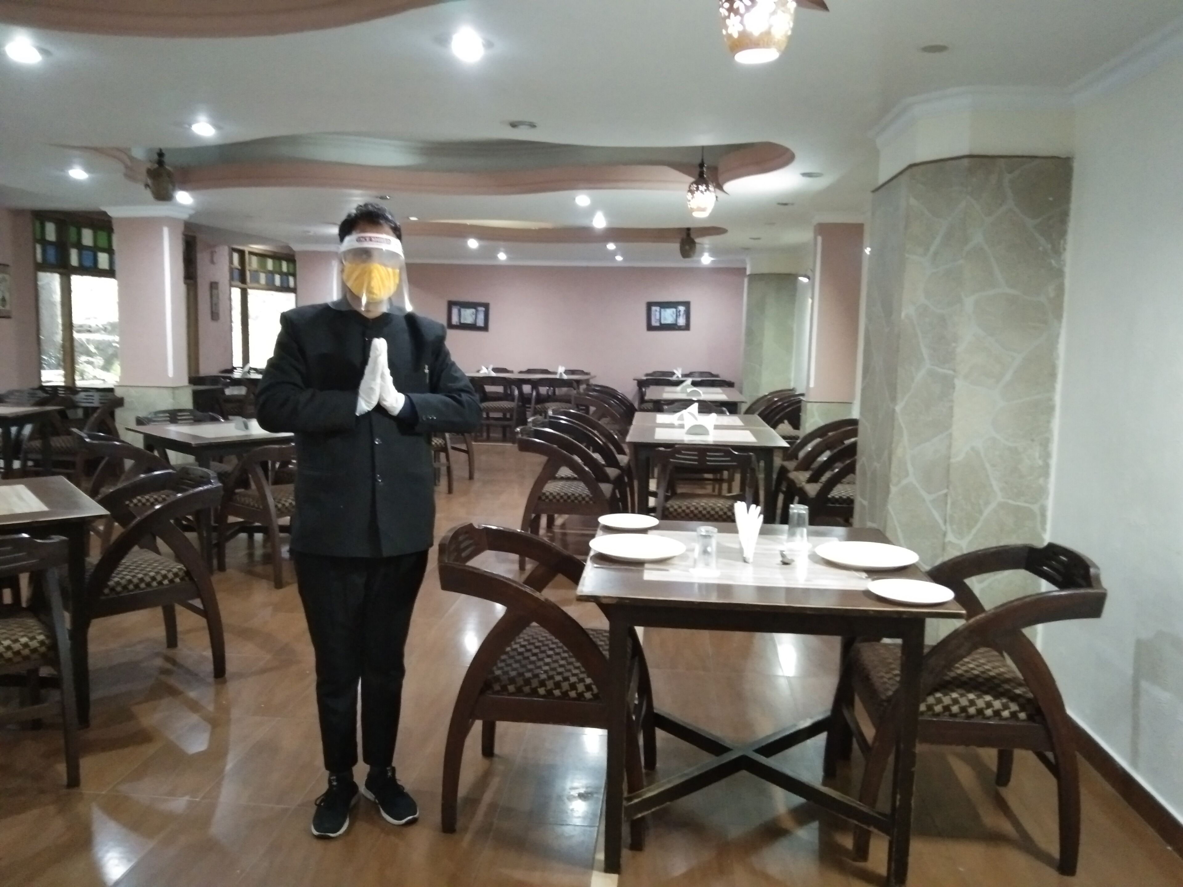 A restaurant with wooden tables and chairs, a person standing in the center, and a ceiling with recessed lighting.