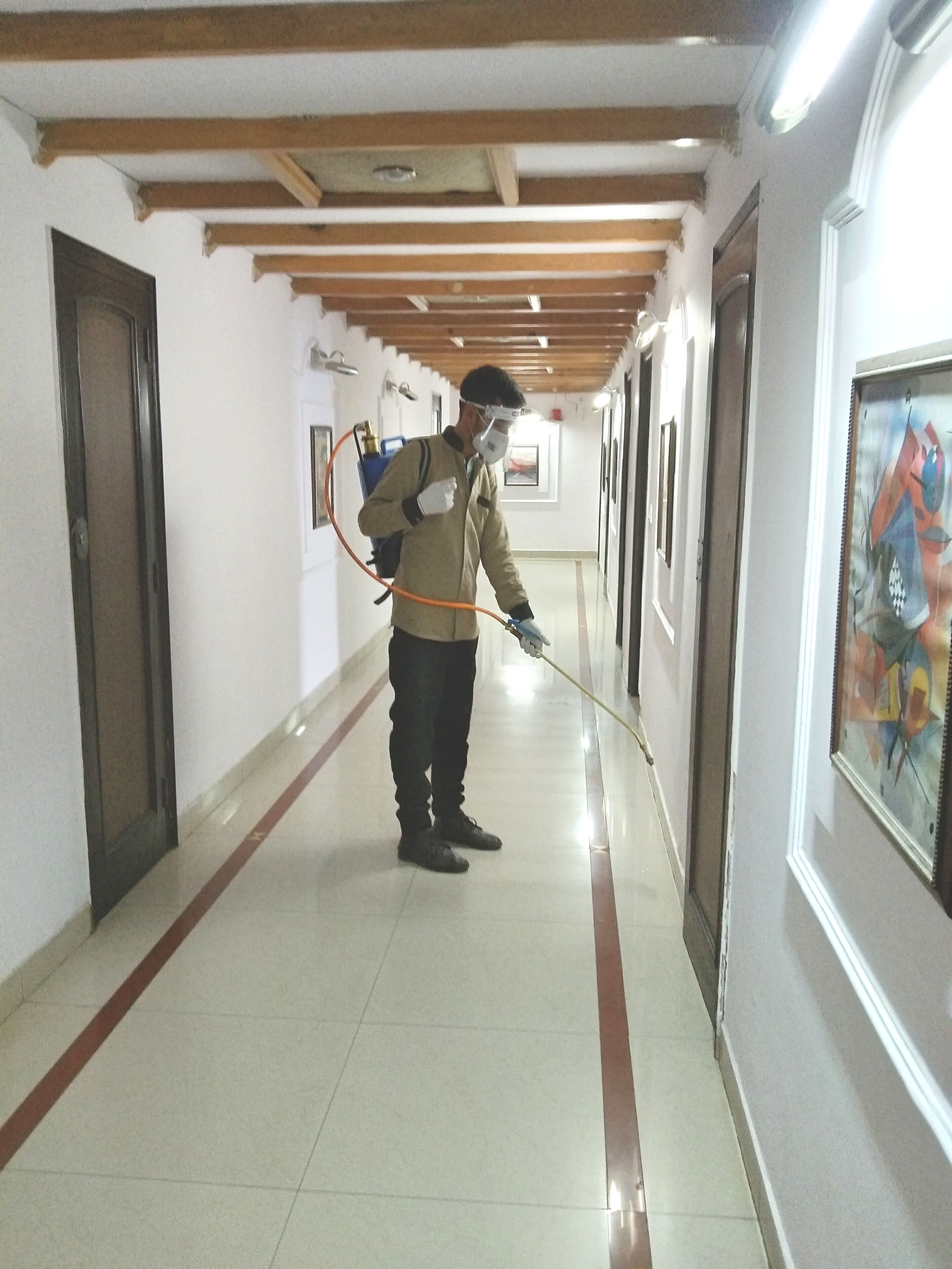 A person in a hallway with wooden beams on the ceiling, tiled floor, and framed artwork on the walls.