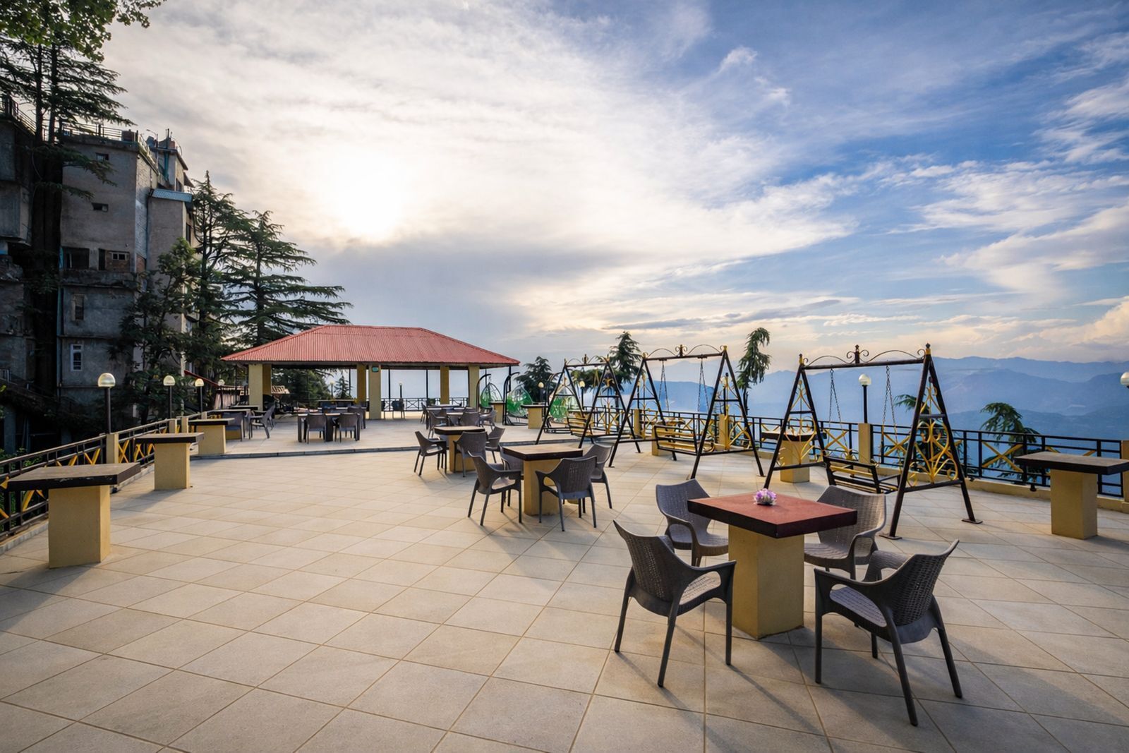 Um terraço com mesas e cadeiras, baloiço e vista para o mar.