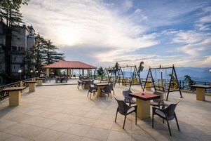 A terrace with tables and chairs, a swing set, and a view of the sea.