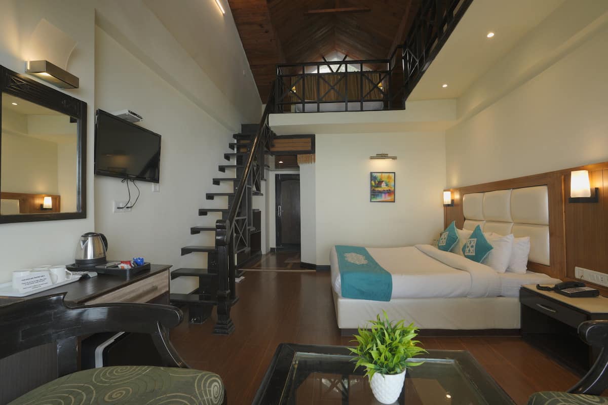 A hotel room with a bed, a desk, a chair, a coffee maker, a TV, and a staircase leading to an upper level.