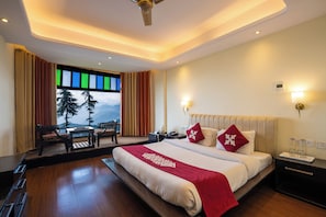 A hotel room with a large bed, a desk, and a view of mountains through the window.