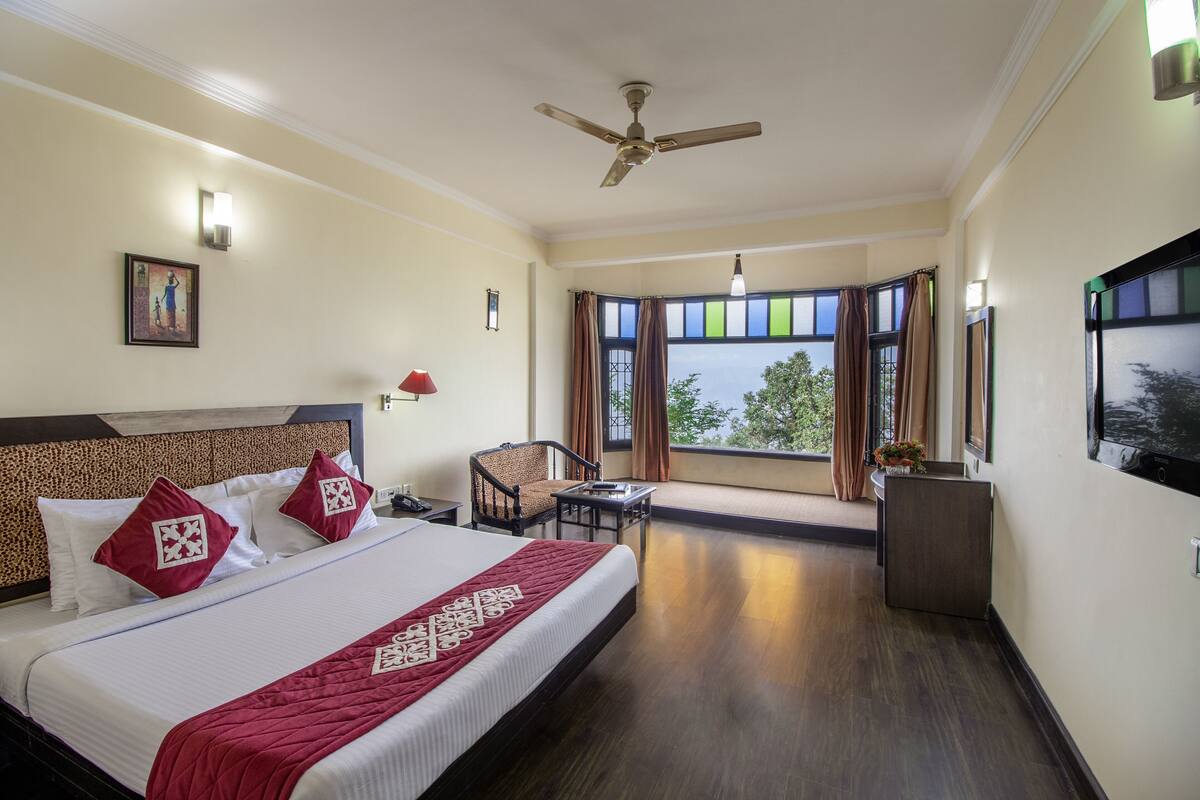 A hotel room with a bed, a desk, a chair, a ceiling fan, and a large window with curtains.