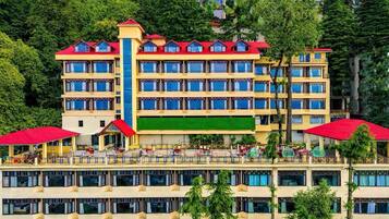 Un hotel de varios pisos con tejado rojo, balcones y un toldo verde.