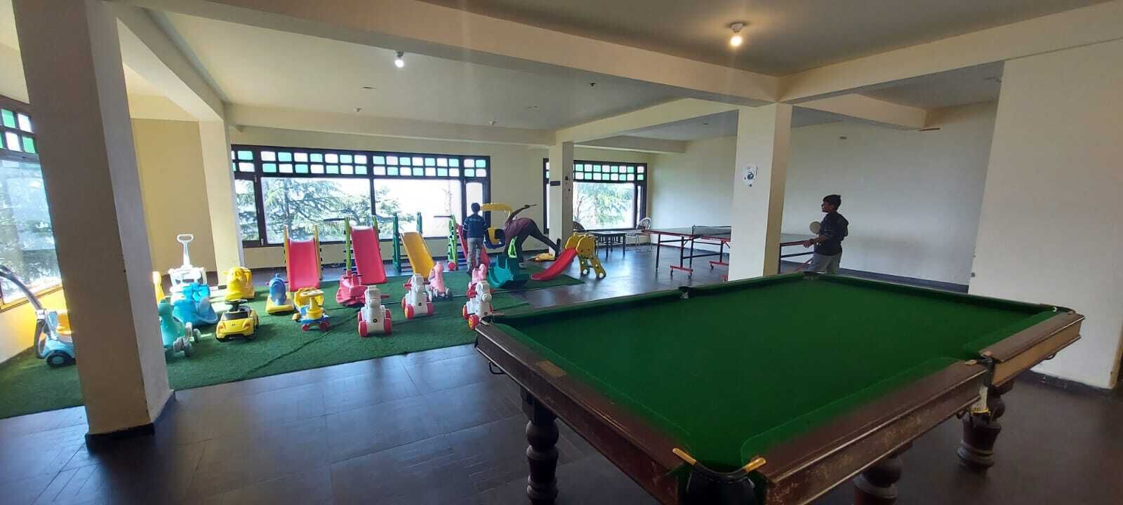 Una sala recreativa con mesa de billar, juegos infantiles y ventanas amplias.