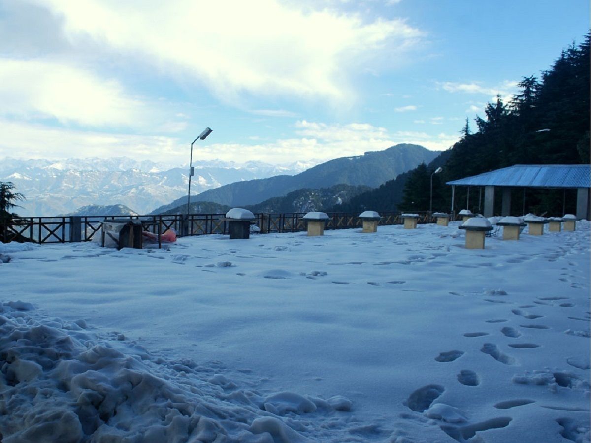 Un paysage enneigé avec une clôture en bois, un lampadaire et plusieurs bâtiments recouverts de neige.