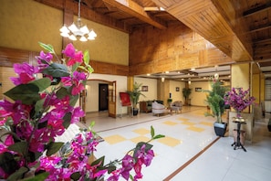 A spacious lobby with wooden ceiling beams, a checkered floor, and potted plants.
