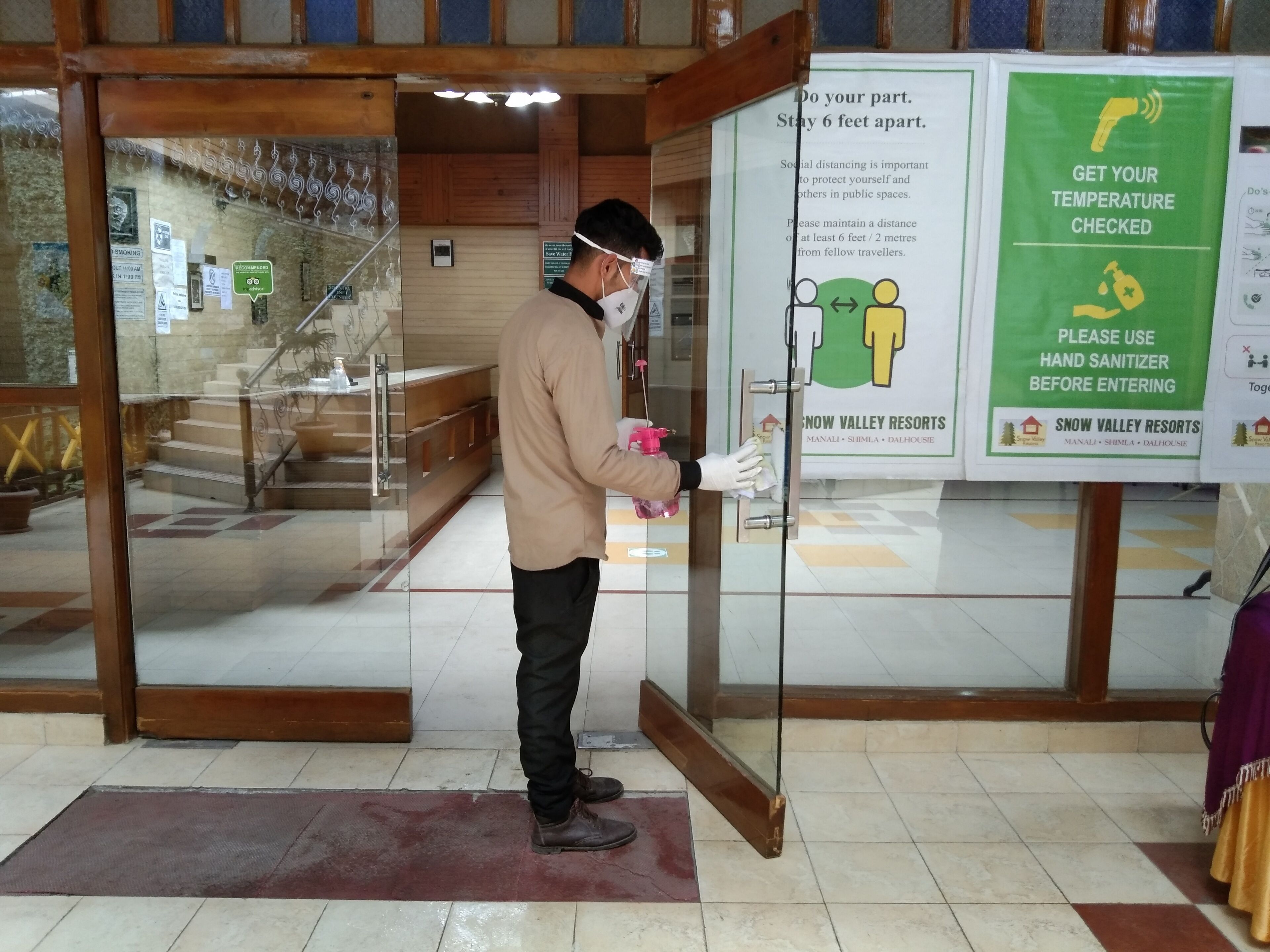 Une personne nettoie une porte vitrée à l’entrée d’un complexe hôtelier.