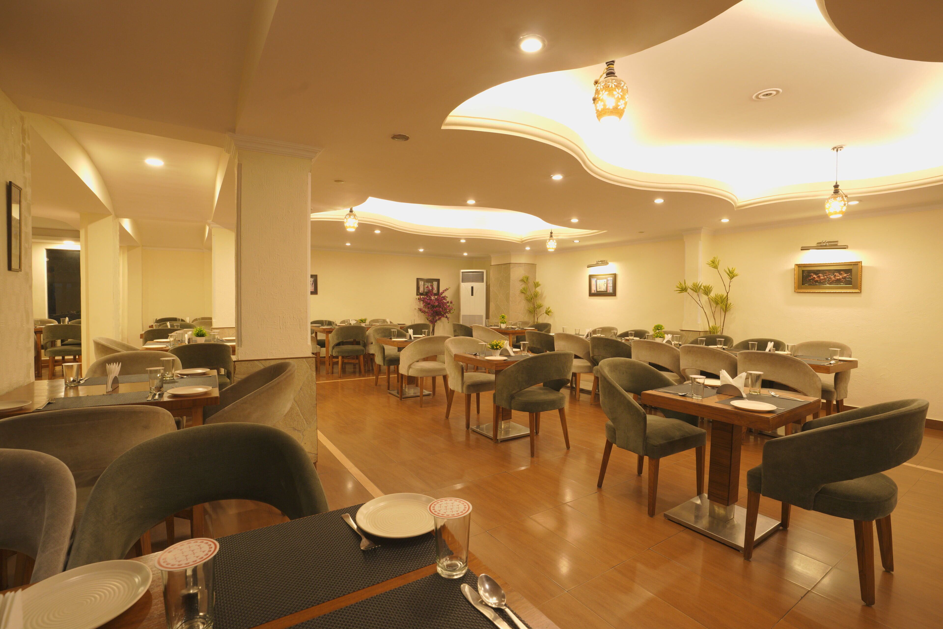 A spacious dining area with multiple tables and chairs, a modern ceiling design, and ambient lighting.