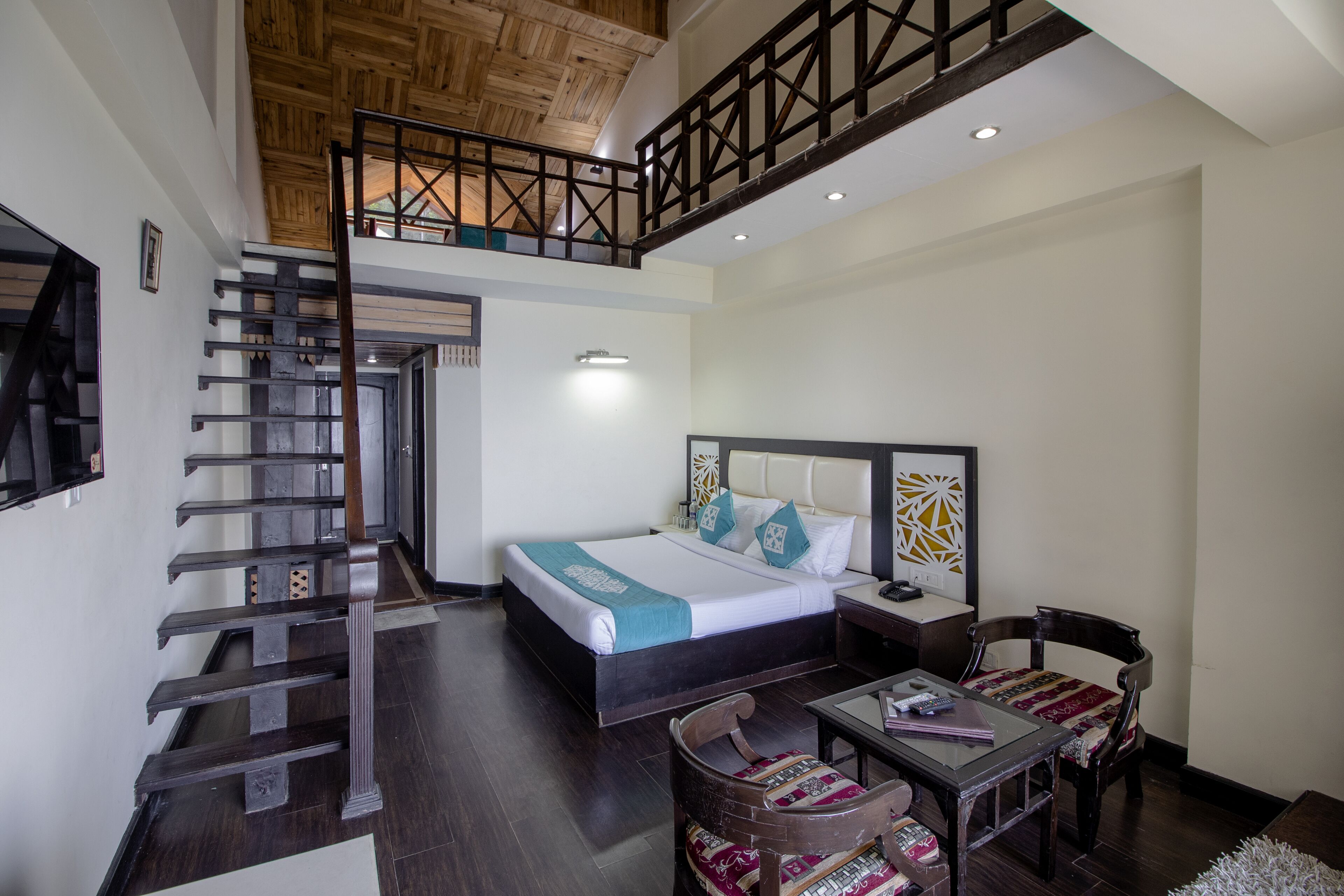 Une chambre d’hôtel avec un lit, un bureau, une chaise, un escalier et un balcon.
