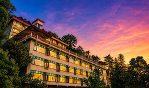 A multi-story hotel with balconies, large windows, and a view of trees.