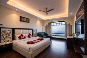 A modern hotel room with a large bed, a ceiling fan, a TV, and a view of the city through the window.