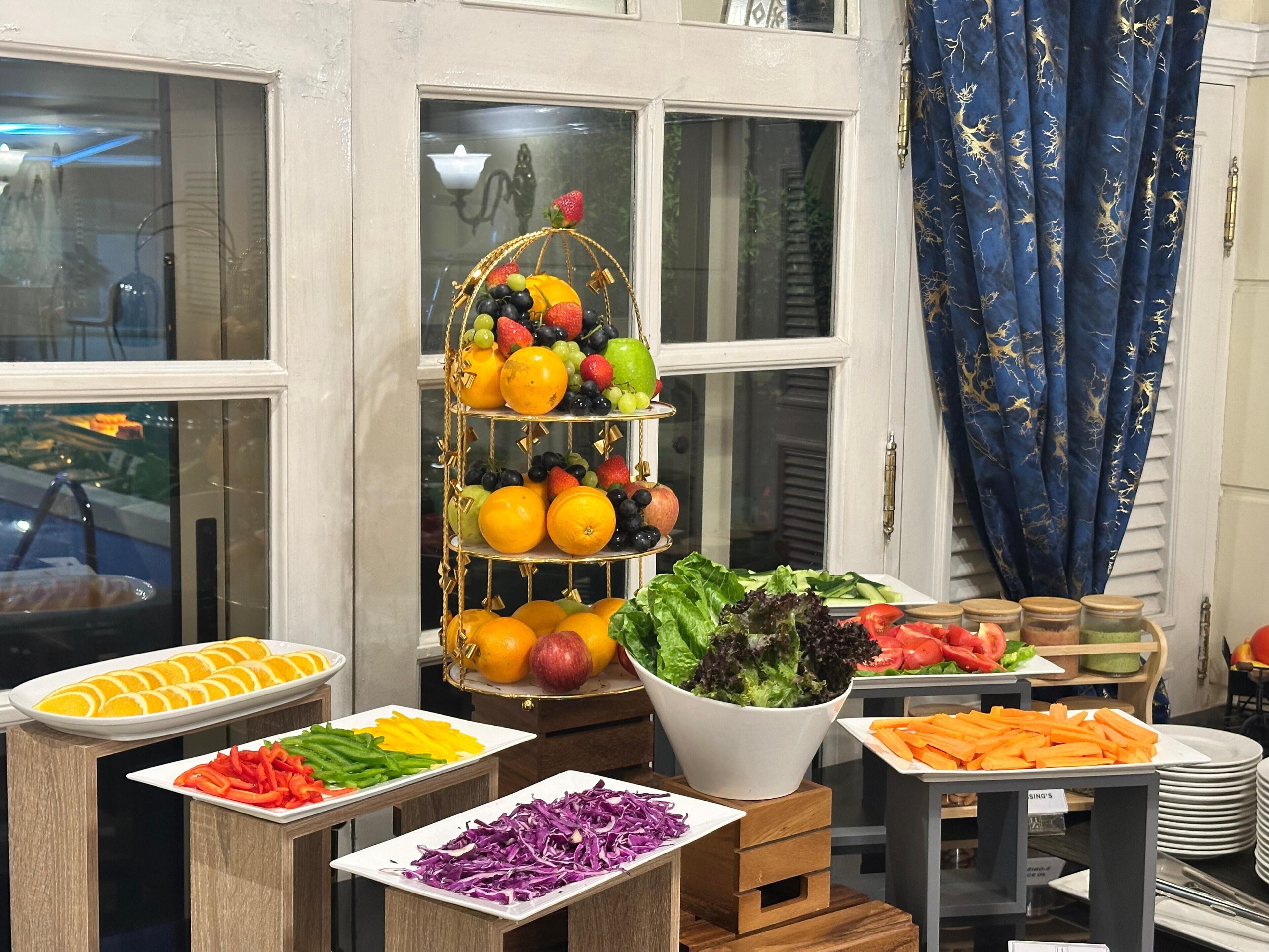 A buffet setup with various food items including fruits, vegetables, and salads.