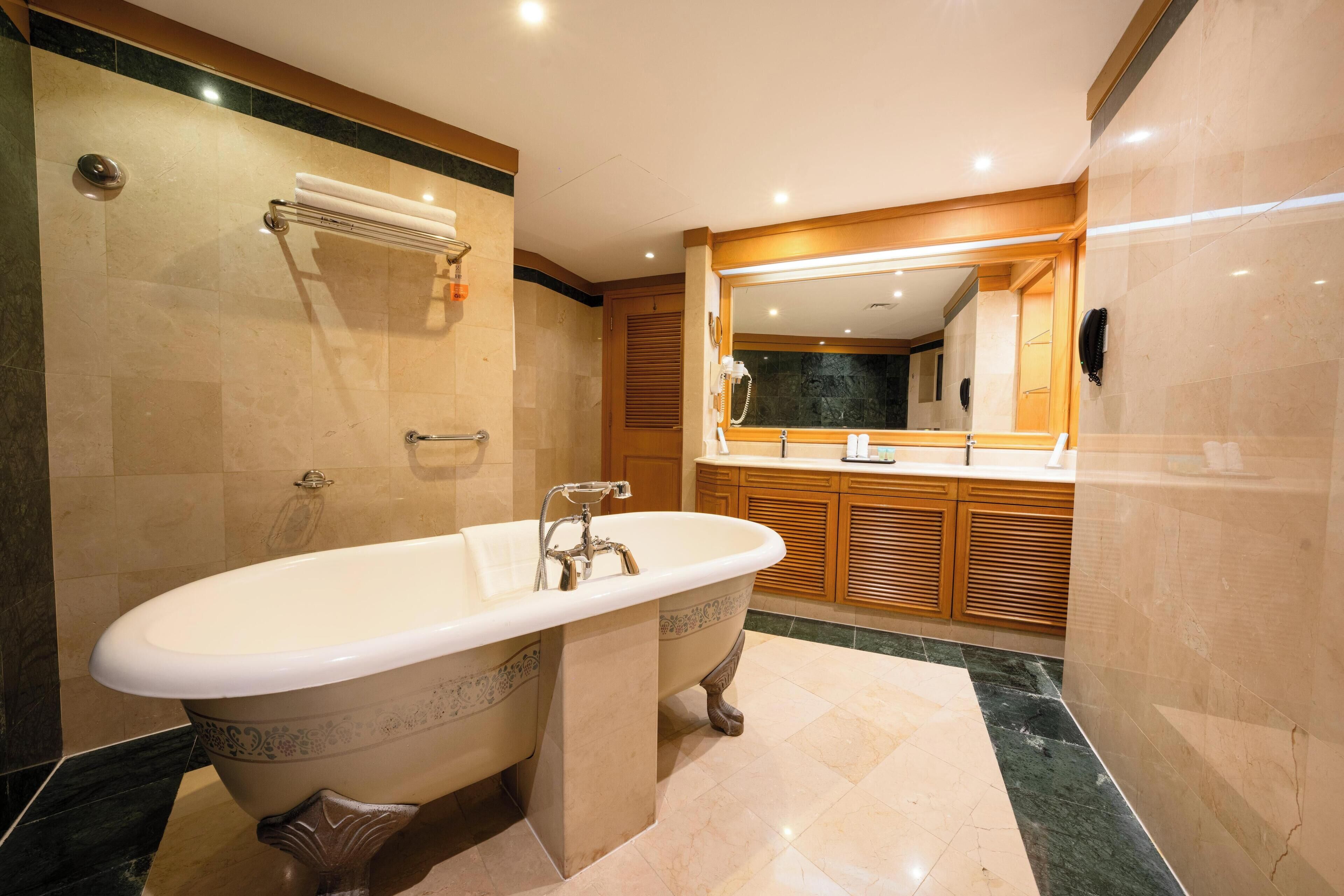 A modern bathroom with a freestanding bathtub, a large mirror, and wooden cabinetry.