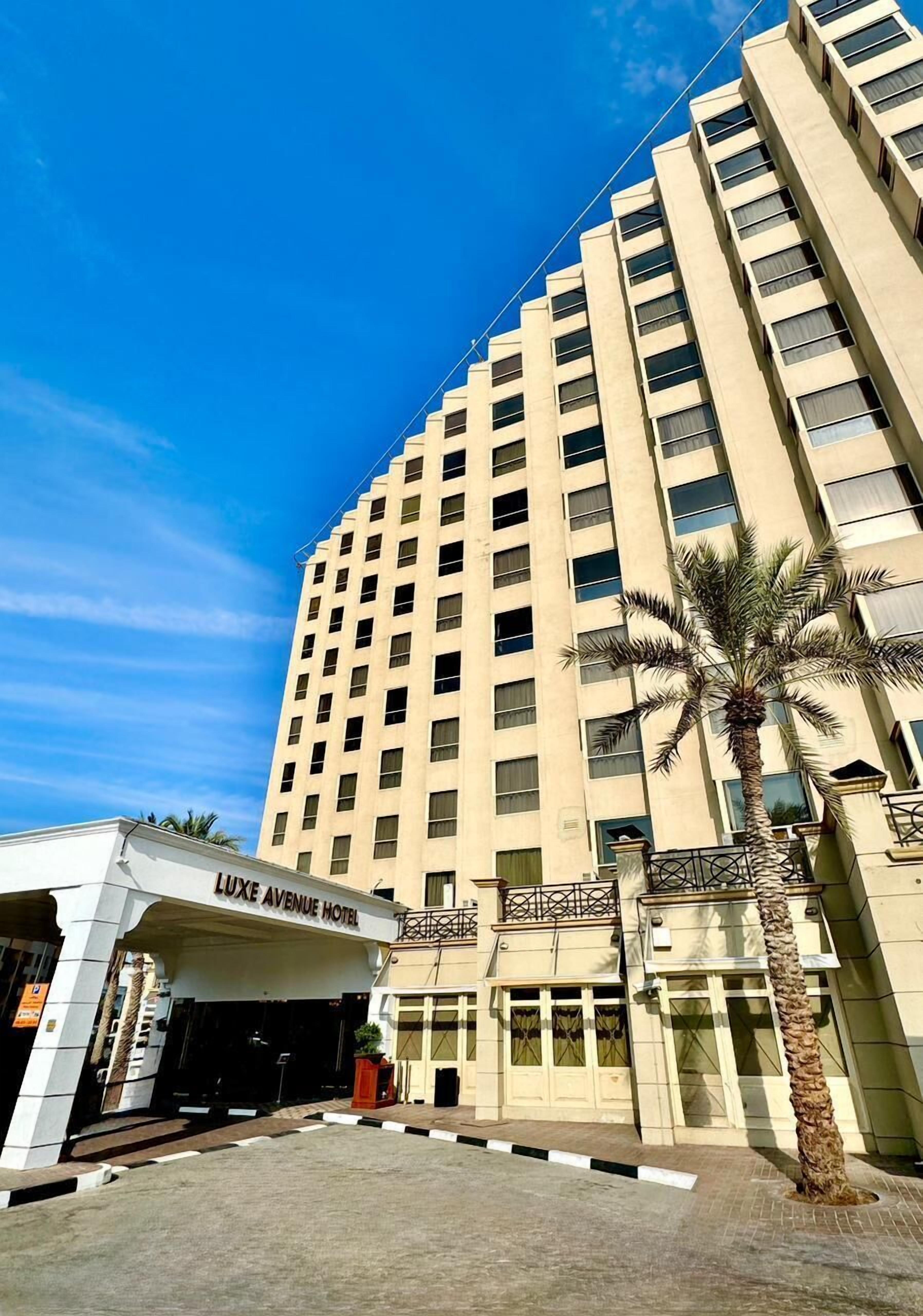 Un edificio alto y color beige de varios pisos con un letrero que dice 'LUXE AVENUE HOTEL' en la entrada.