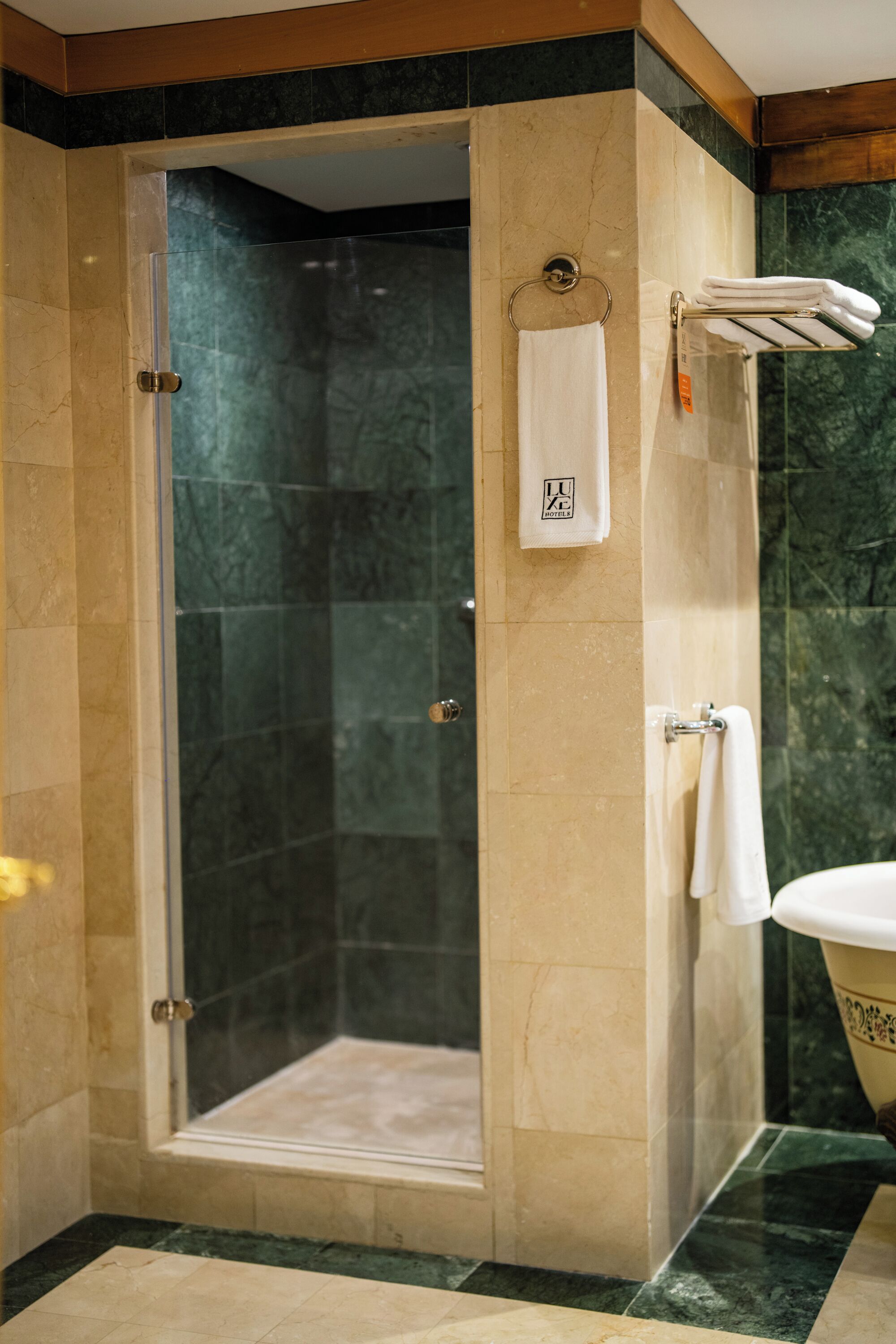 Un área de ducha con puerta de vidrio, un perchero con una toalla blanca y una bañera con un lavamanos decorativo.
