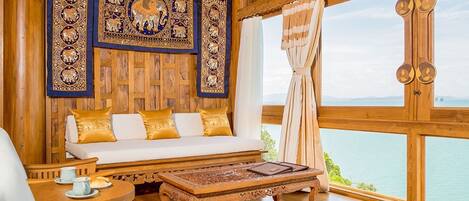 A wooden interior with a sofa, a table, and a view of the sea.