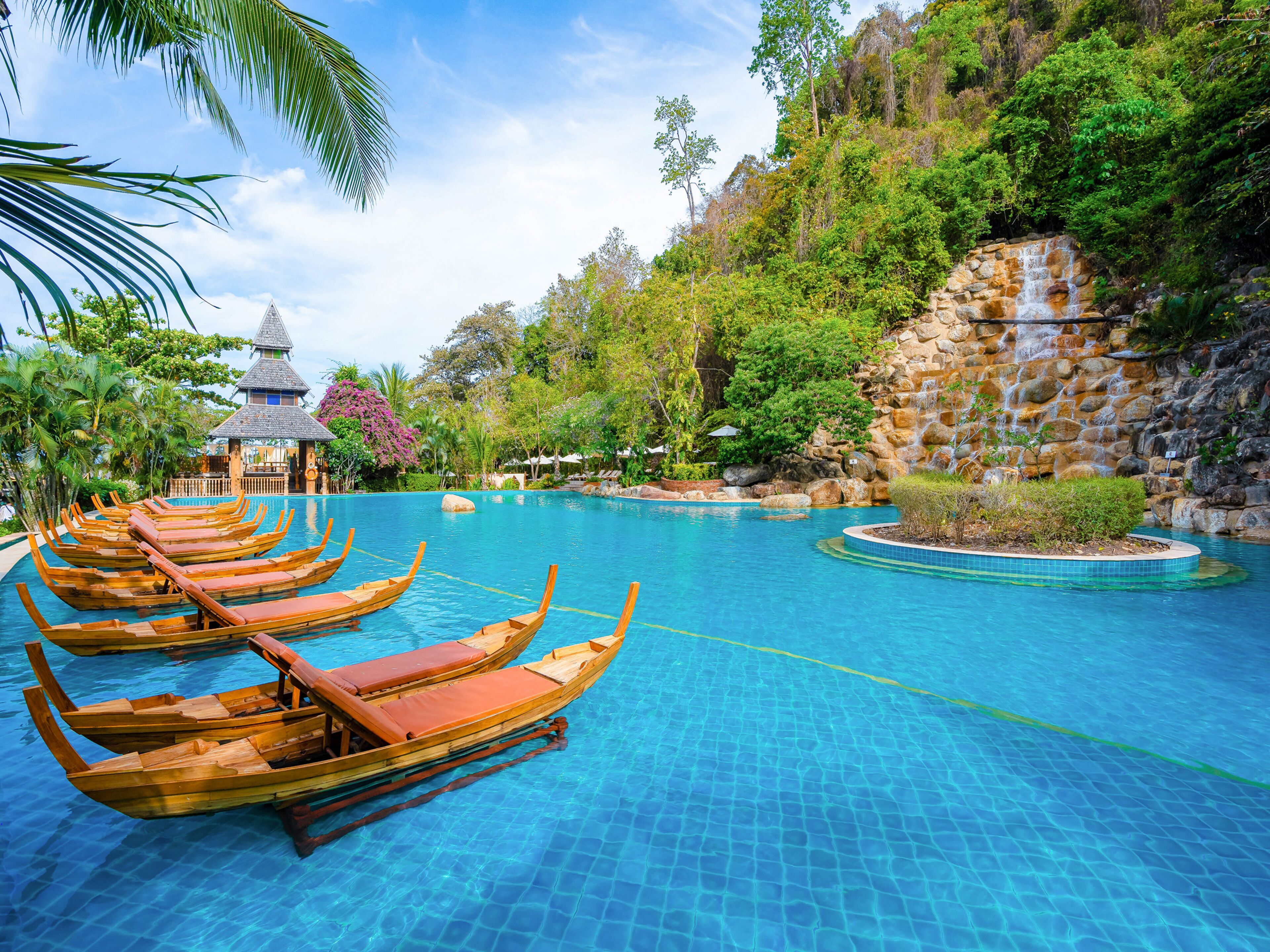 Ein Pool mit Holzbooten, einer Laube und üppigem Grün.
