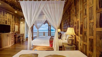 A four-poster canopy bed with a view of the sea, wooden paneling, a television, and a lamp on a bedside table.