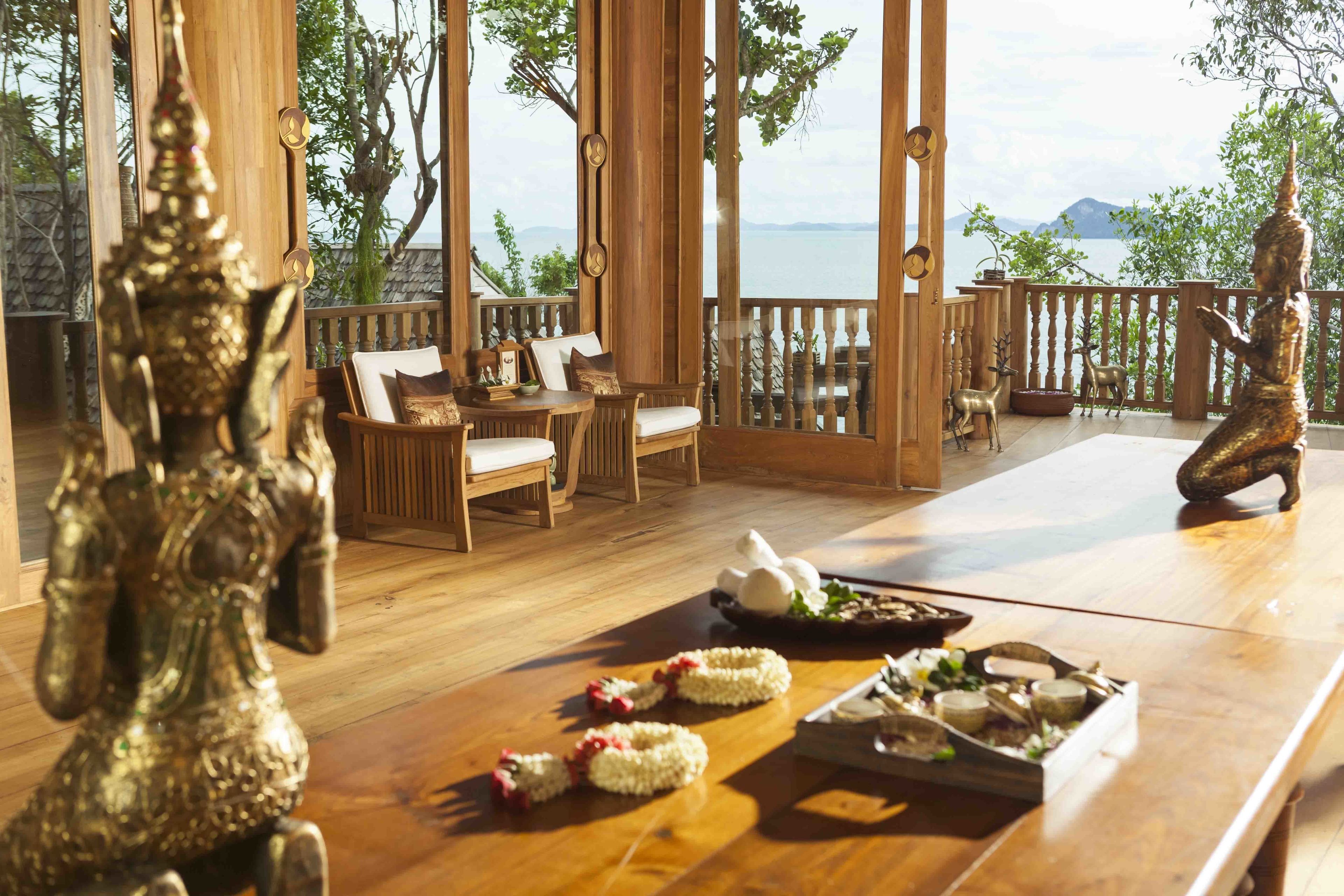 A wooden deck with a table set for dining, surrounded by wooden chairs and a decorative statue.