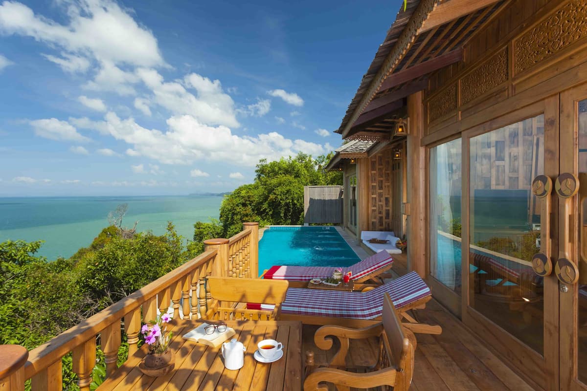 A wooden deck with a pool, lounge chairs, and a table with drinks and flowers.