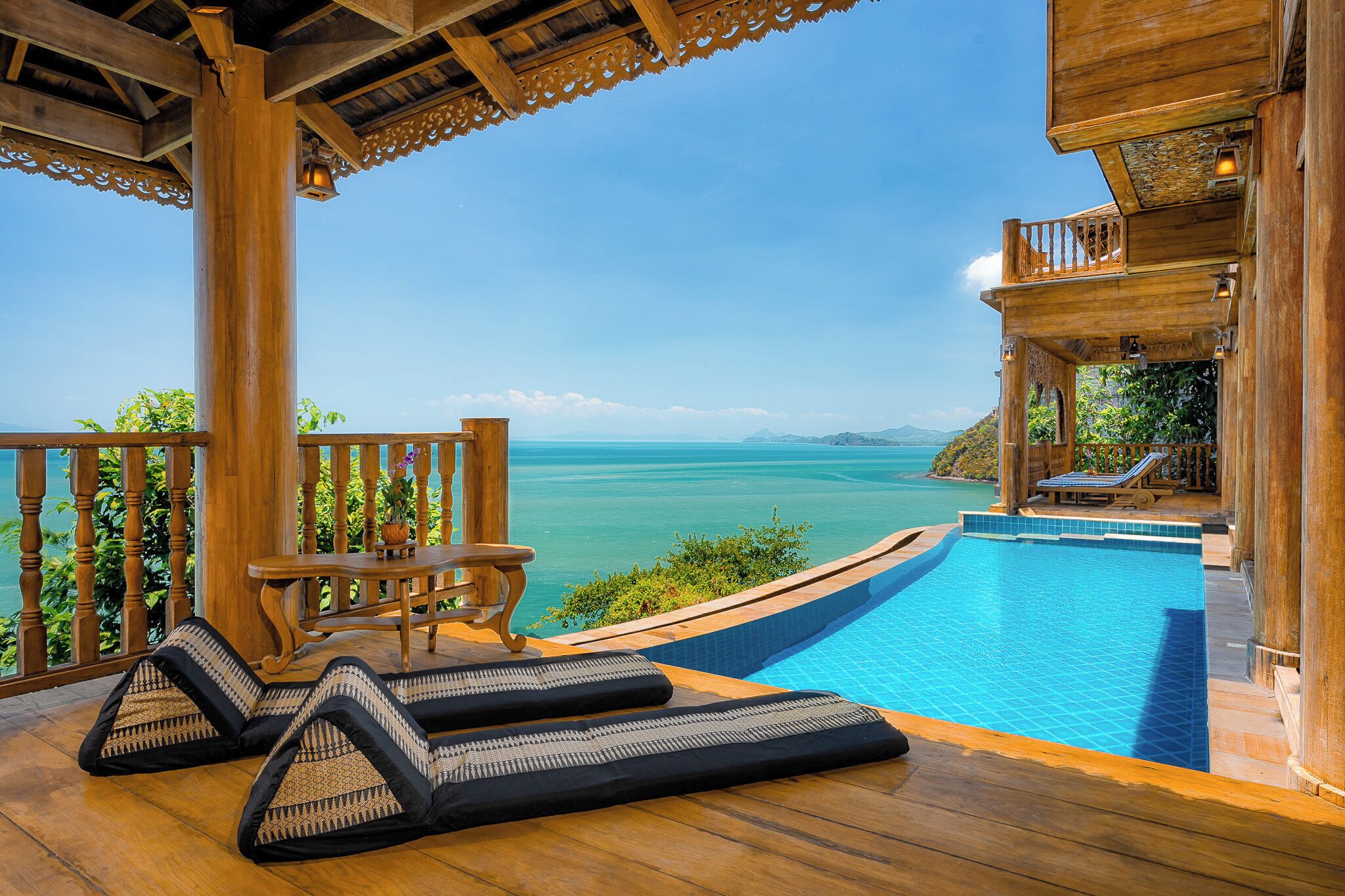 A wooden deck with a pool, lounge chairs, and a view of the sea.