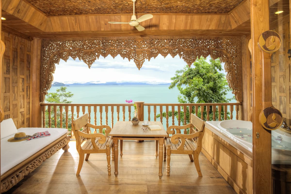 A wooden balcony with a table and chairs, a bed, and a view of a body of water.