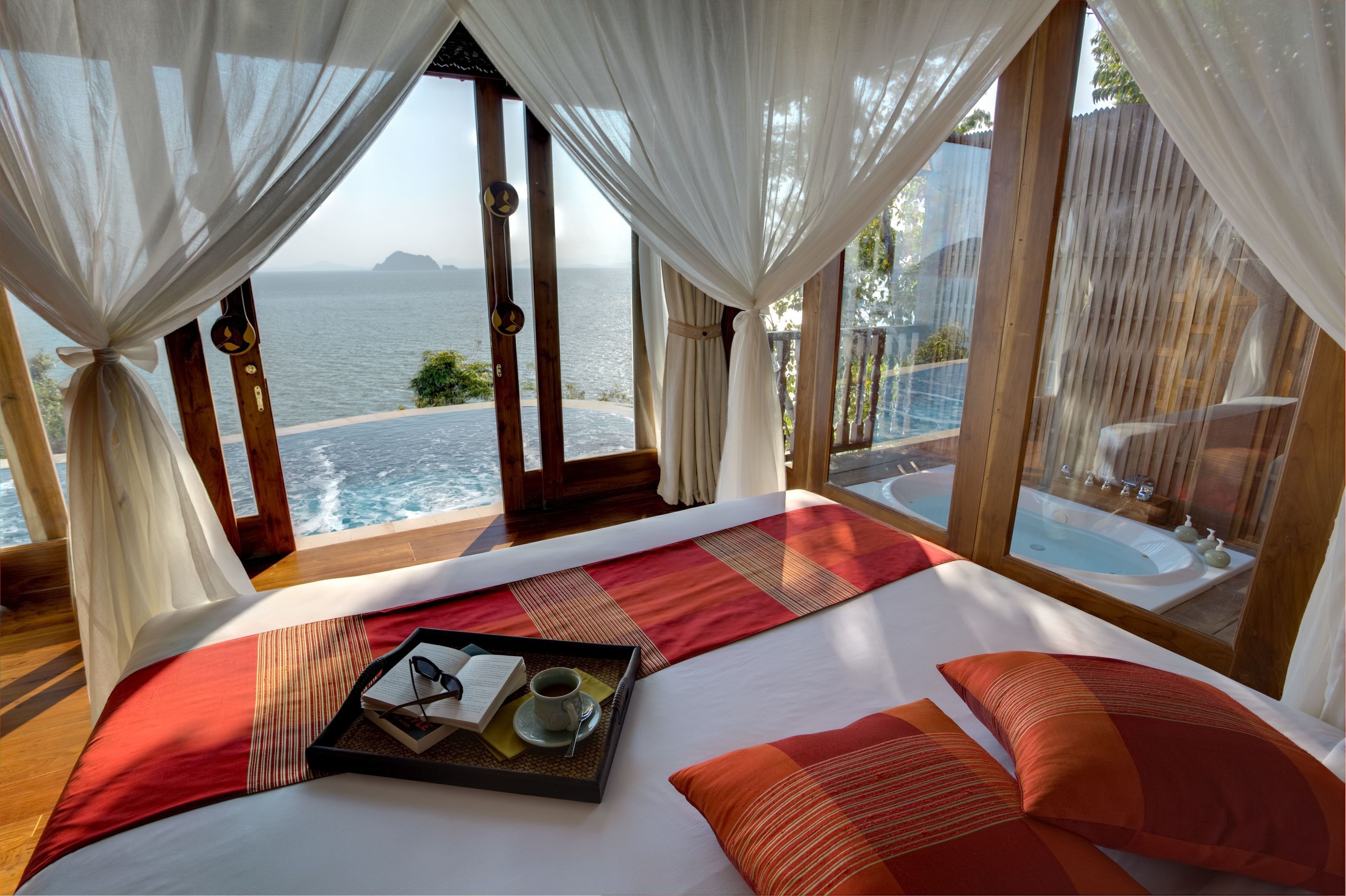 A bedroom with a large bed, a tray with a book and cup, and a view of the sea.