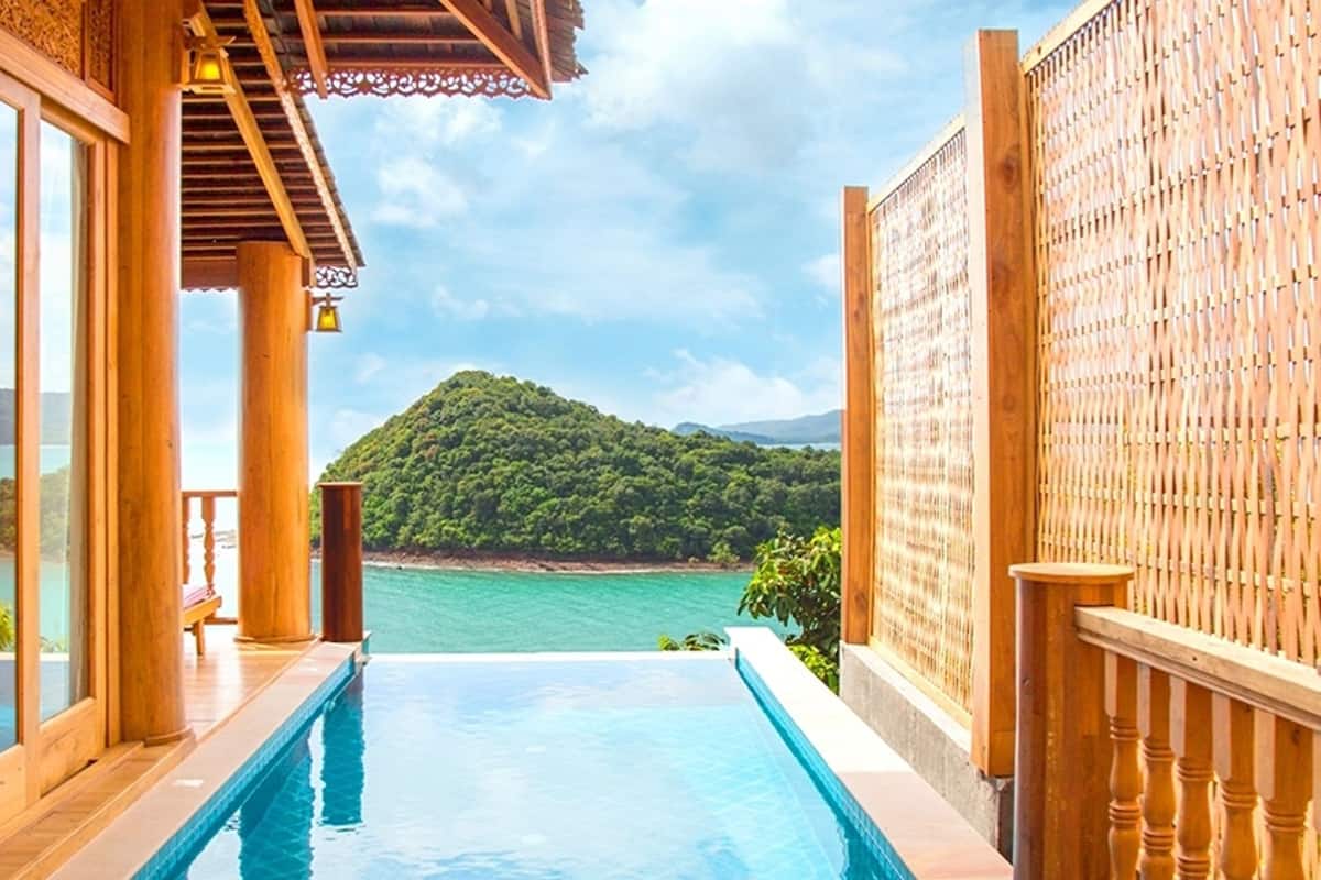 A poolside view with a wooden deck, glass doors, and a view of a mountain and sea.