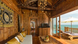 Interior de madera con un sofá, una mesa con fruta, un televisor y un balcón con vista al mar.