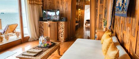 A wooden-floored living area with a sofa, television, and a view of the sea.