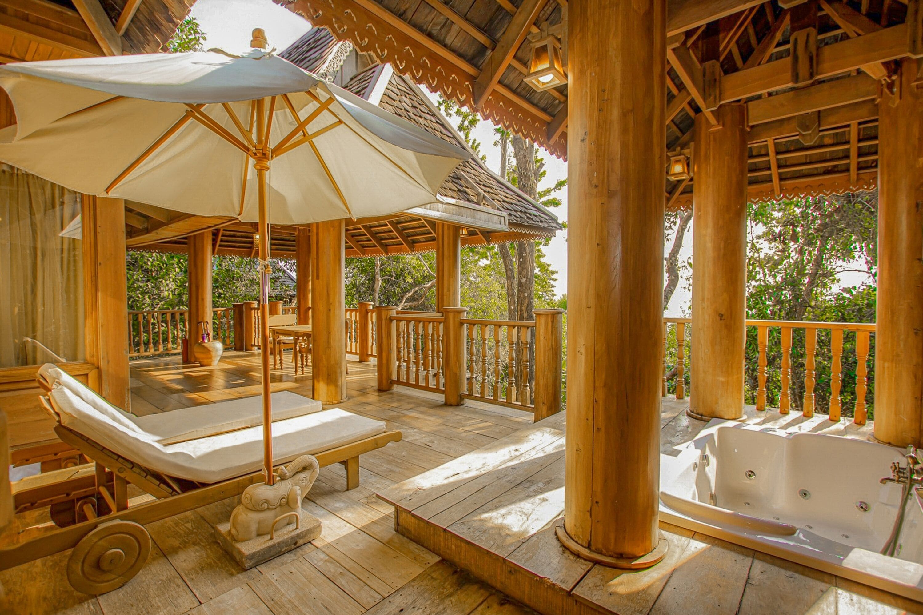A wooden deck with a sun lounger, a large umbrella, and a hot tub.