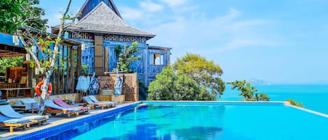 Un resort con piscina, sillones de descanso y vista al océano.