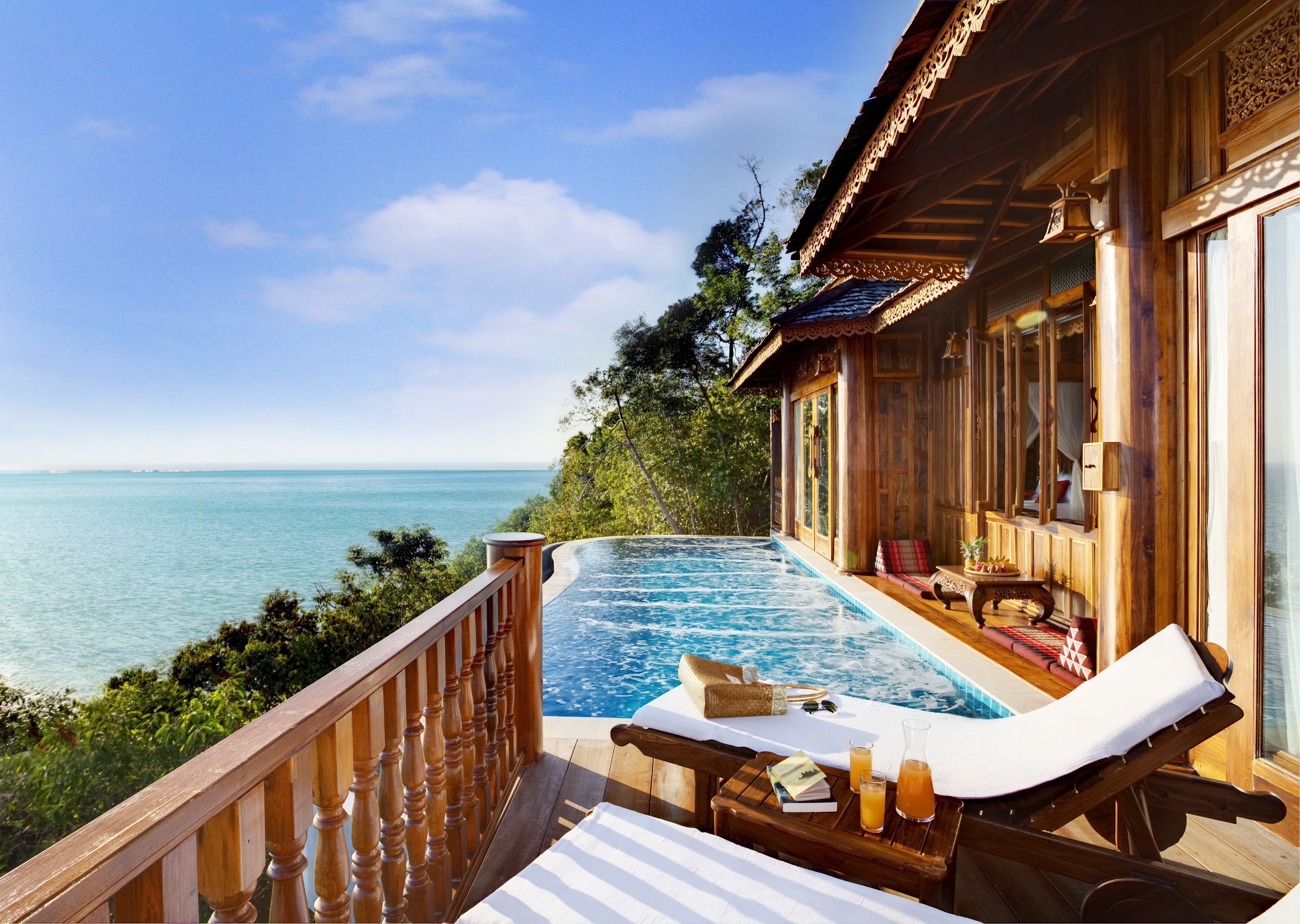 Una terraza de madera con piscina, sillas de descanso y vista al mar.