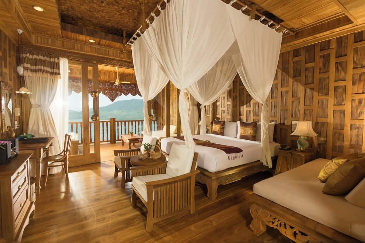 A room with a four-poster bed, wooden furniture, and a balcony with a view.