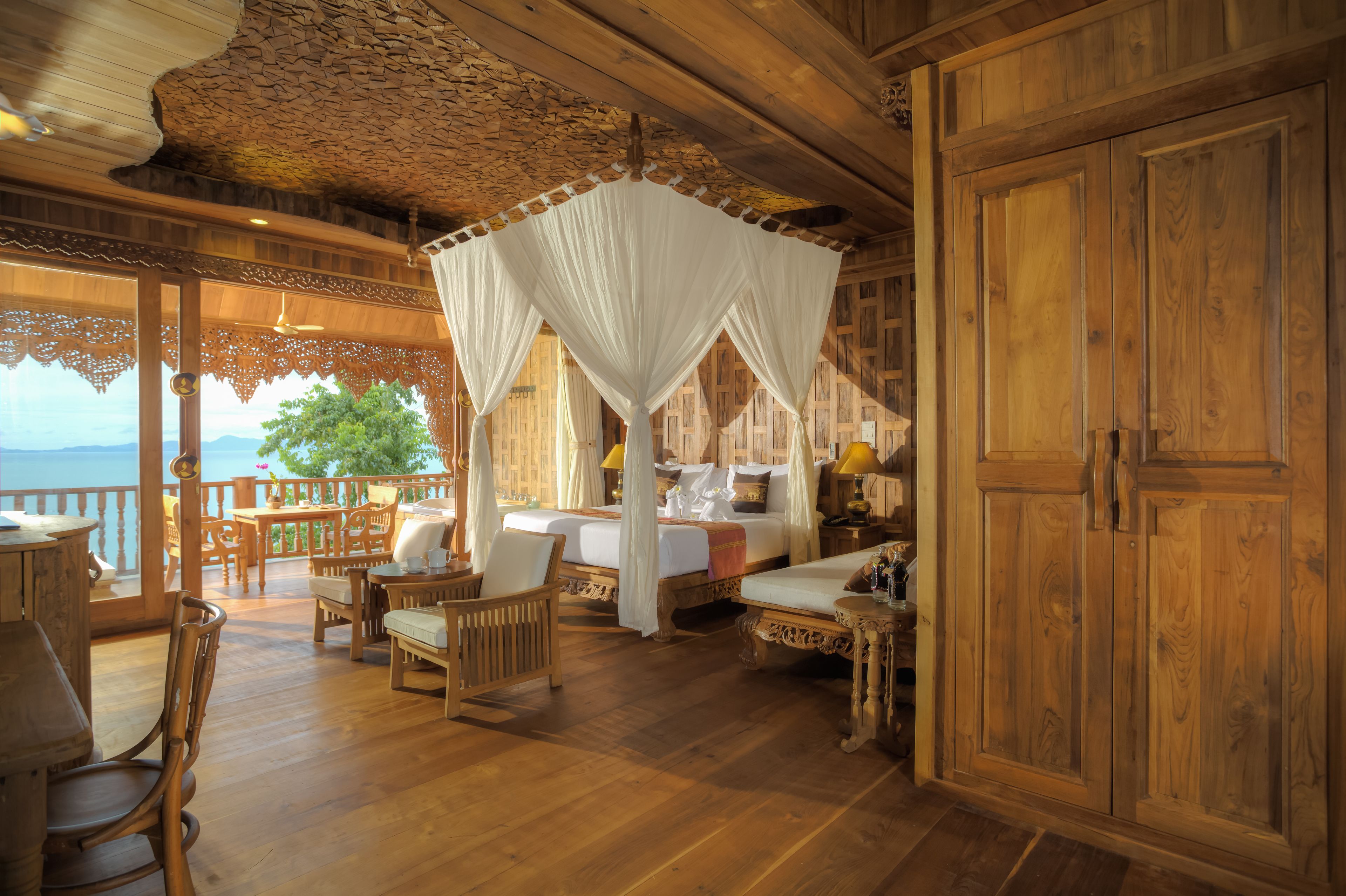 A wooden cabin with a balcony, furnished with wicker chairs and a bed with a canopy.