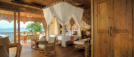 A wooden cabin with a balcony, furnished with wicker chairs and a bed with a canopy.
